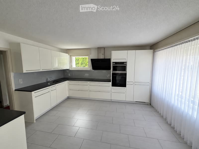 Modern kitchen with white cabinets, black countertops, and tiled flooring. Features a sink, oven, microwave, and a window with curtains.