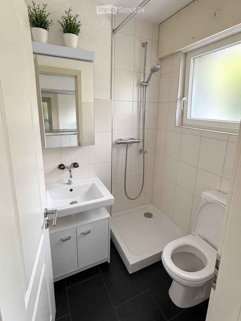 Modern bathroom with white tiles, black floor, sink, toilet, bathtub, mirror, and showerhead.