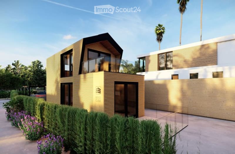 Modern two-story house with a contemporary design, featuring large windows, a flat roof, and a wooden facade. The house is surrounded by a well-maintained garden with shrubs and flowers, and there is a neighboring building visible in the background.