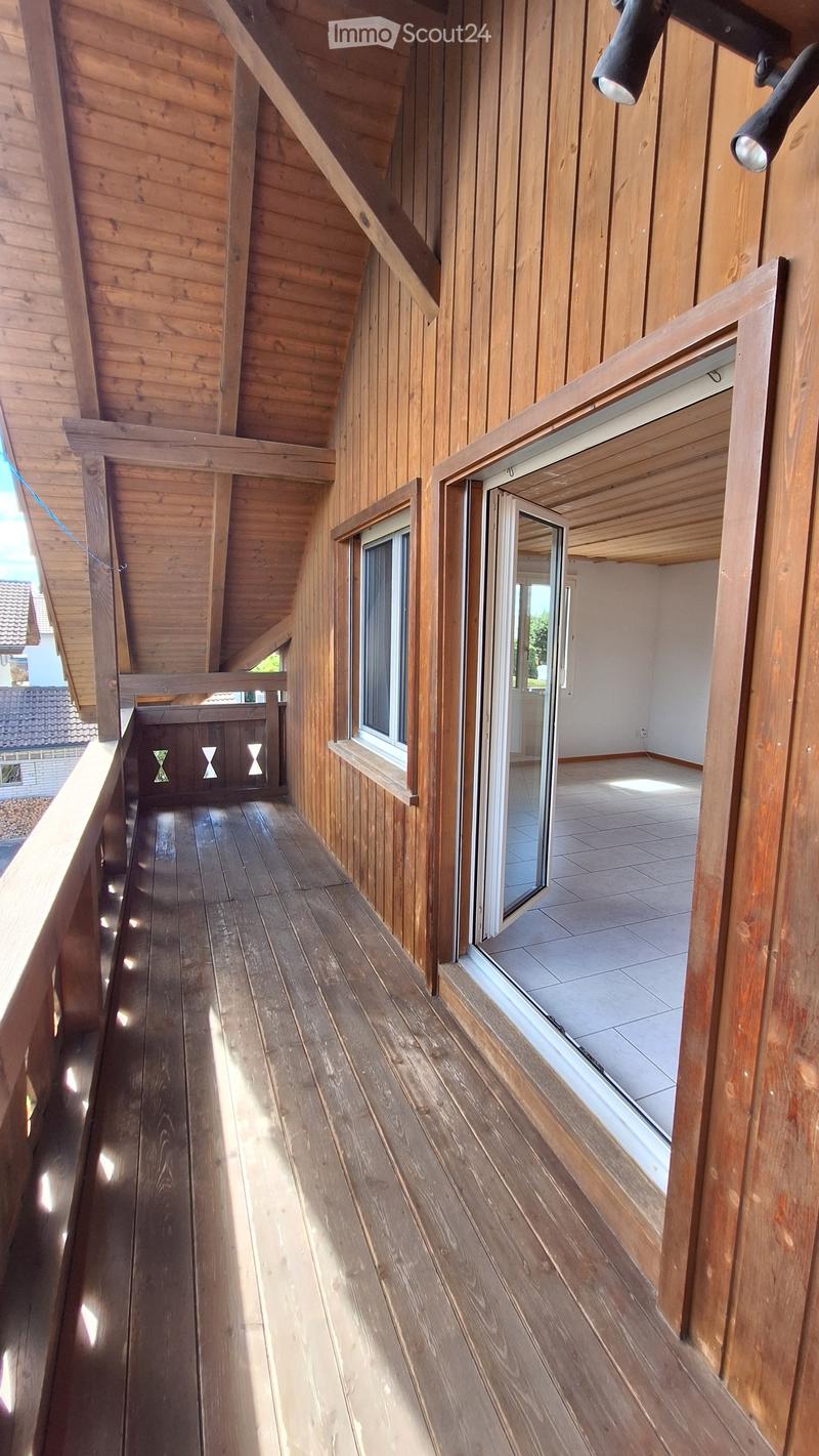 Wooden balcony with slanted wooden ceiling, large windows, and open sliding doors leading to an interior space.