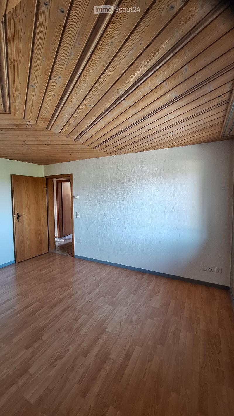 Empty room with wooden flooring, light-colored walls, and a wooden door leading to another space.