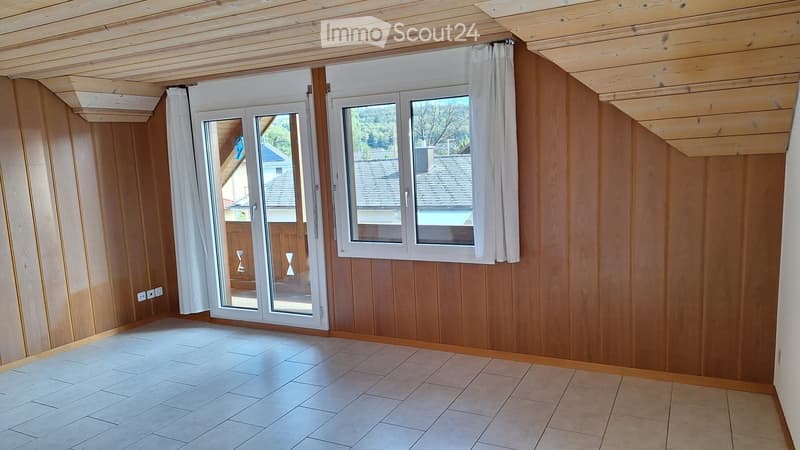 Empty room with wooden walls, white tiled floor, large window with white curtains, and a sliding glass door leading outside.