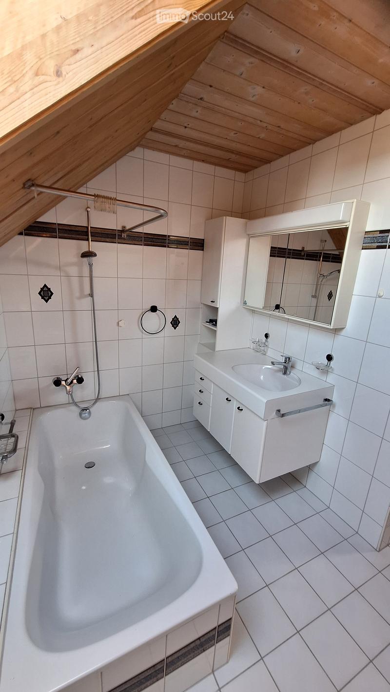 Modern bathroom with white tiled walls and floor, featuring a bathtub, sink with cabinet, and a mirror above the sink.