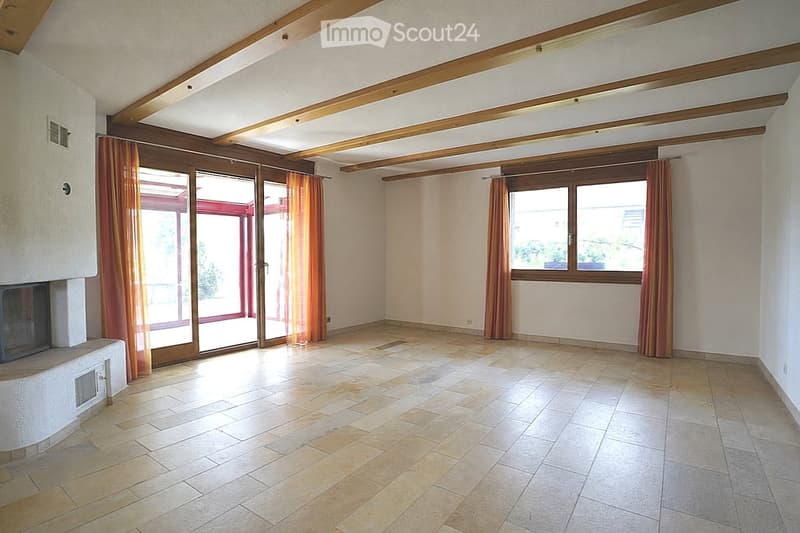 Empty room with tiled floor, wooden ceiling beams, large windows, and sliding glass doors leading to a patio.