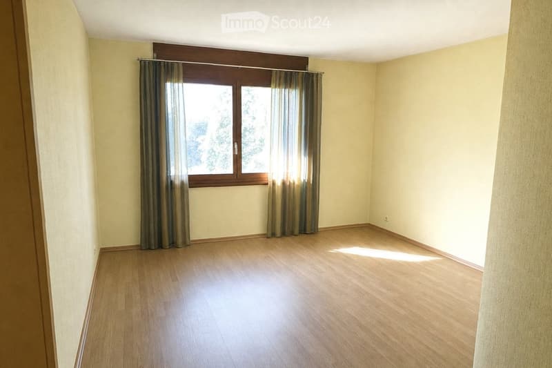 Empty room with light yellow walls, wooden flooring, and a large window with curtains. No furniture or equipment is present.