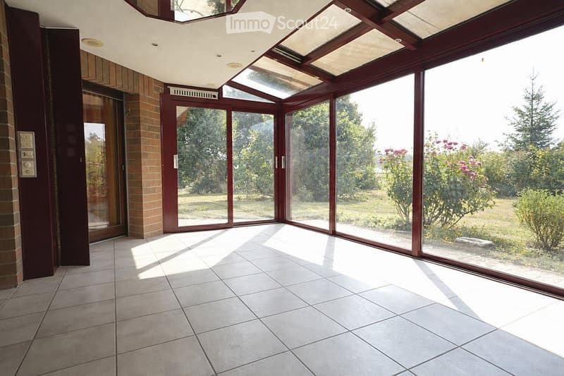 Bright, empty room with large glass windows and sliding doors, tiled floor, and a brick wall on one side.