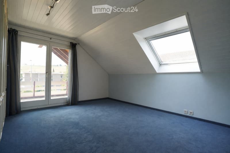 Empty attic room with blue carpet, white paneled ceiling, skylight window, and sliding glass doors leading to a balcony.