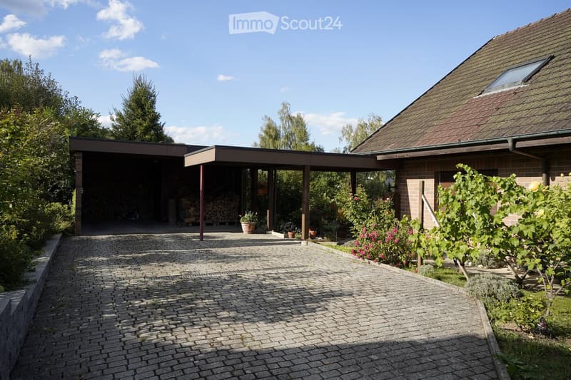 Brick-paved pathway leading to a modern house with a covered garage and garden area featuring various plants and flowers.