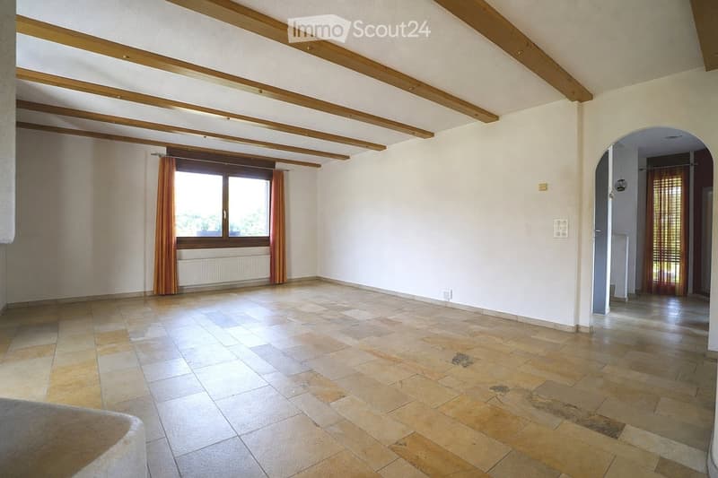 Empty room with tiled floor, white walls, wooden ceiling beams, large window with curtains, and an arched doorway leading to another space.