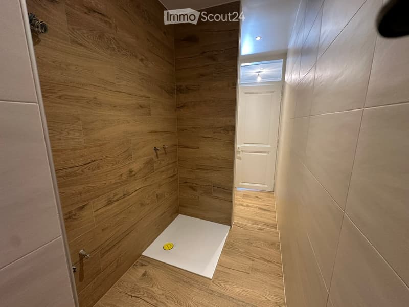 Modern hallway with wooden flooring and walls, featuring a white door and a small white platform with a yellow circular object on it.