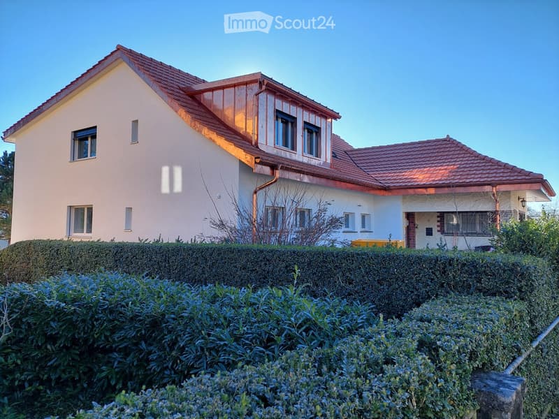Two-story house with red-tiled roof, white walls, multiple windows, and a well-maintained hedge in the front yard.