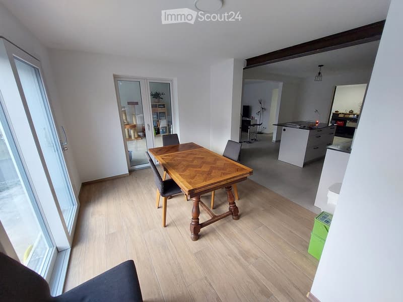 Open-plan dining and kitchen area with wooden flooring, a wooden dining table with four chairs, a cat tree in the corner, and a modern kitchen island with stools.