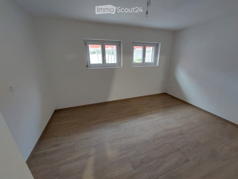 Empty room with wooden flooring and white walls, featuring two windows with white frames and a single ceiling light fixture.