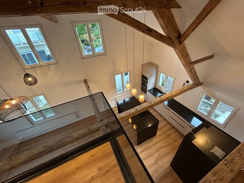 Modern kitchen with wooden beams, pendant lights, and a black kitchen island.