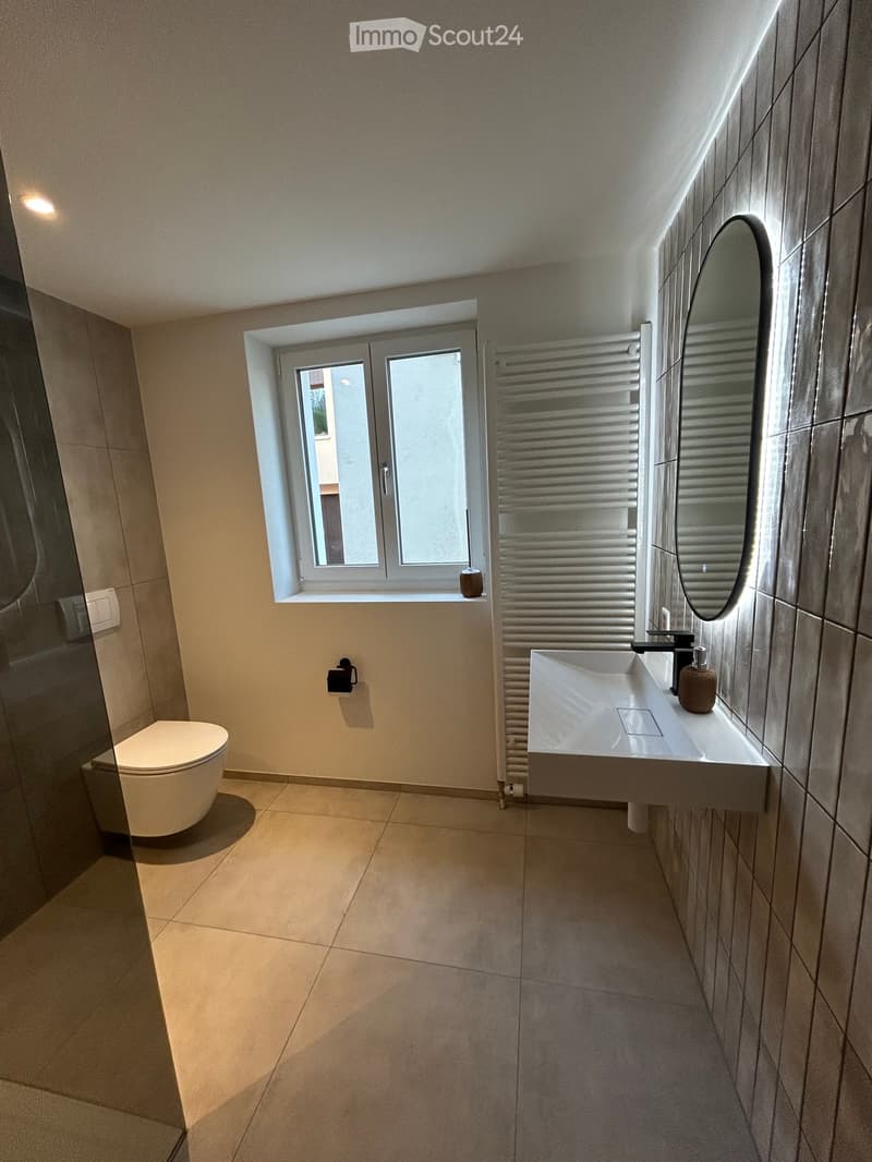 Modern bathroom with a toilet, sink, mirror, and radiator. Features a large window with frosted glass and a sleek, contemporary design.