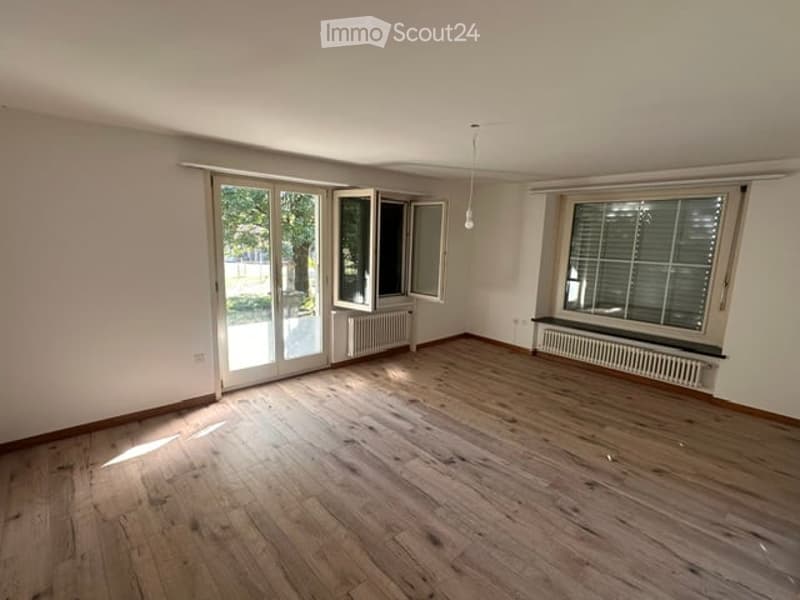 Completely empty room with wooden flooring, large windows, and sliding glass doors leading to an outdoor area.