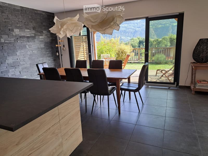 Modern dining area with a wooden dining table, black chairs, a wooden counter, and a large window offering a scenic mountain view.
