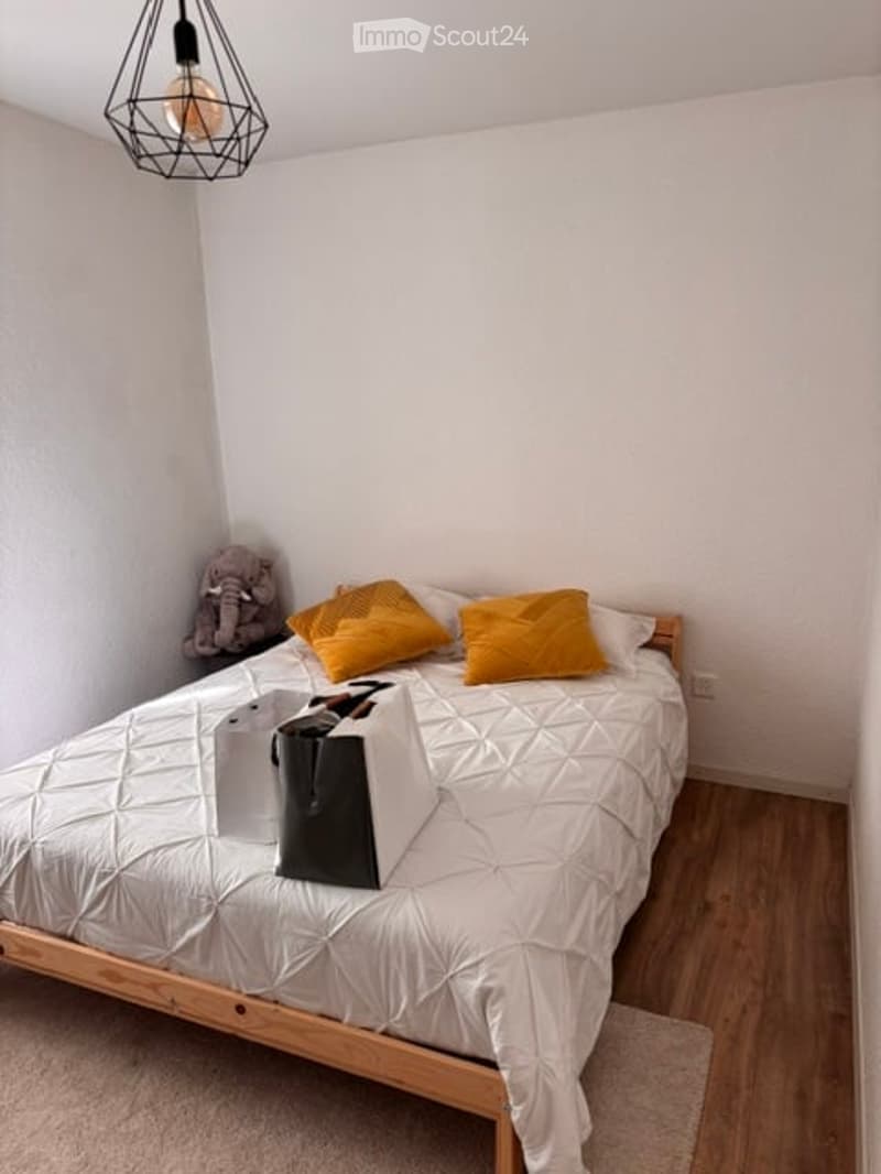 Cozy bedroom with a white quilted bed, yellow pillows, shopping bags, and a small elephant toy on a shelf.