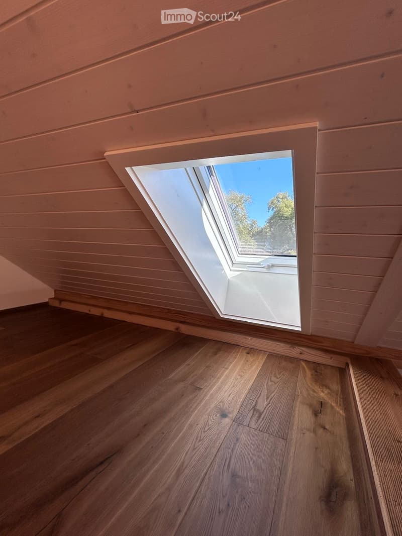 An unfurnished room with wooden flooring and a skylight window offering a view of the outdoors.