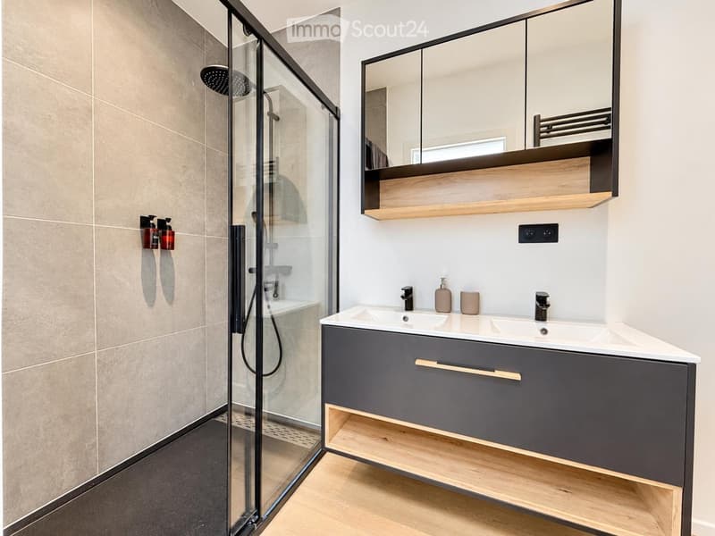 Modern bathroom with a glass-enclosed shower, double sink vanity with mirrored cabinet, and sleek fixtures.
