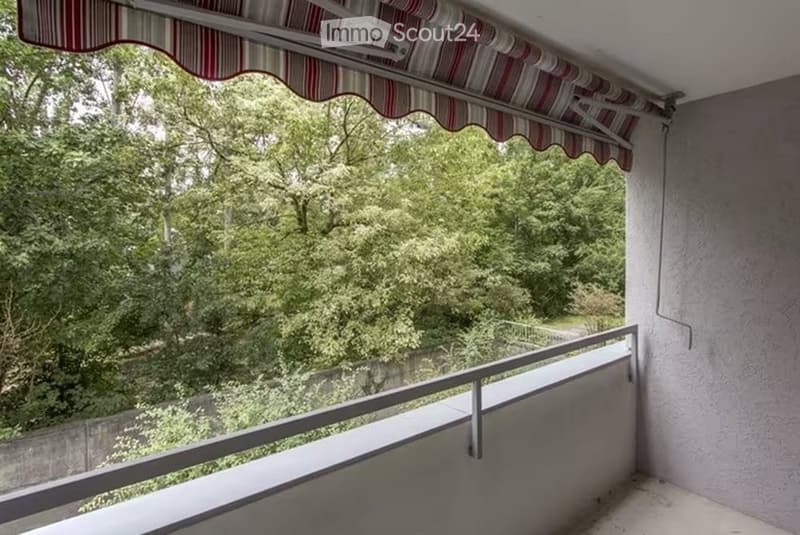 Balcony with striped awning, metal railing, and lush green view of trees and landscape.