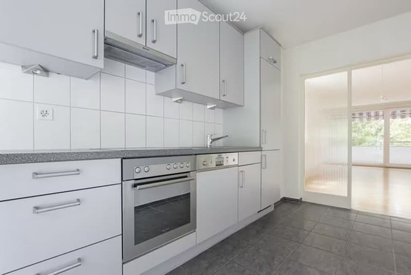 Modern kitchen with white cabinets, stainless steel oven, and a tiled backsplash. Features a sleek design with a large window and a modern faucet.