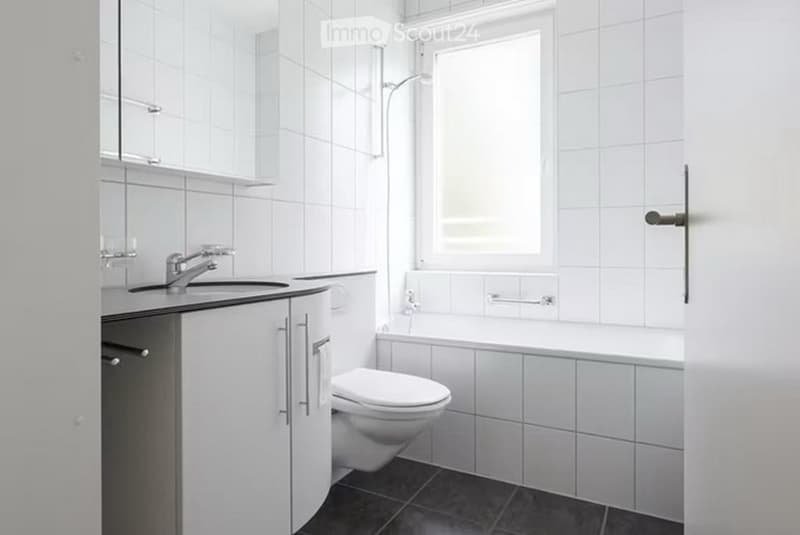 Modern bathroom with white tiled walls and black tiled floor, featuring a sink with faucet, a toilet, a bathtub, and a showerhead.