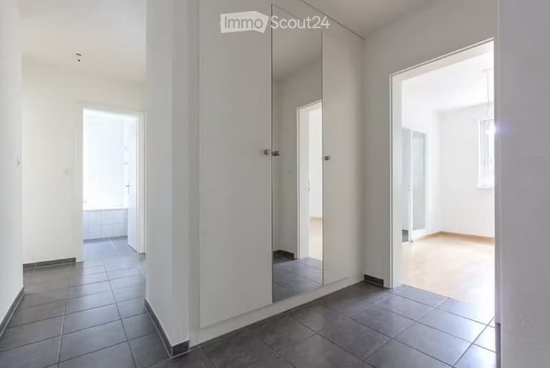 Empty hallway with tiled floor, white walls, and large mirrored closet doors. No furniture or equipment visible.
