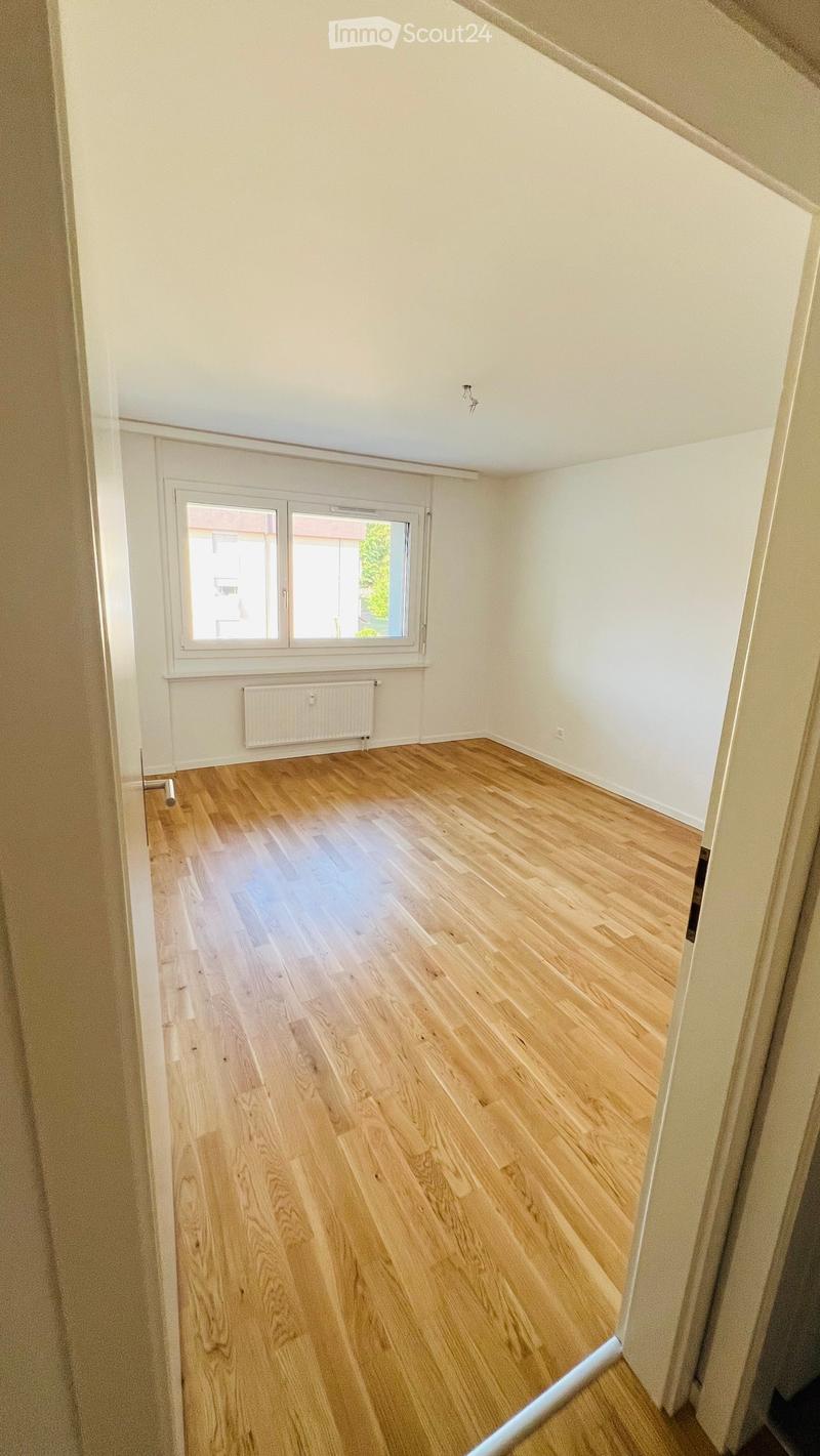 Empty room with light wooden flooring, white walls, and a window with a radiator below it.