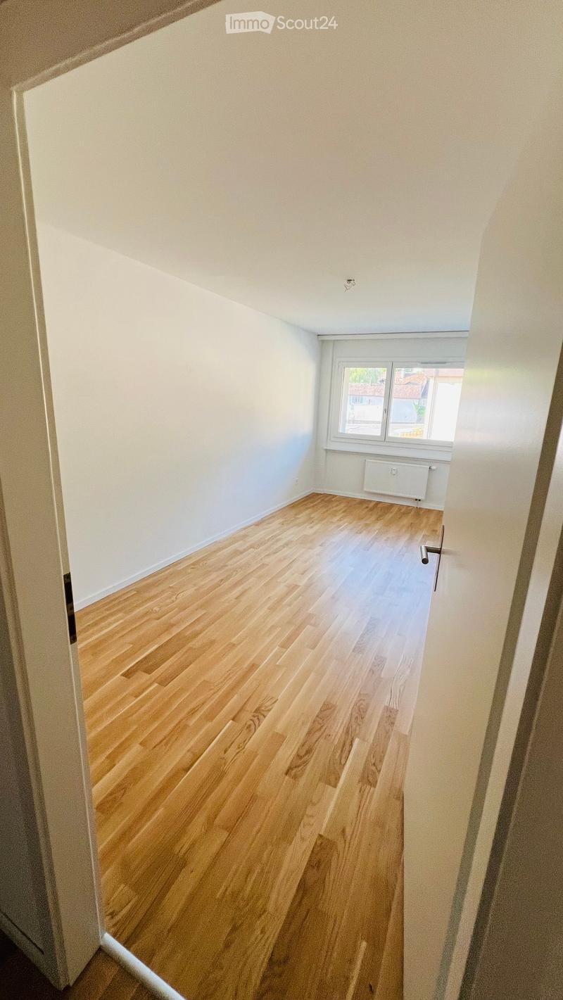 Empty room with wooden flooring, white walls, and a window with a radiator below it.