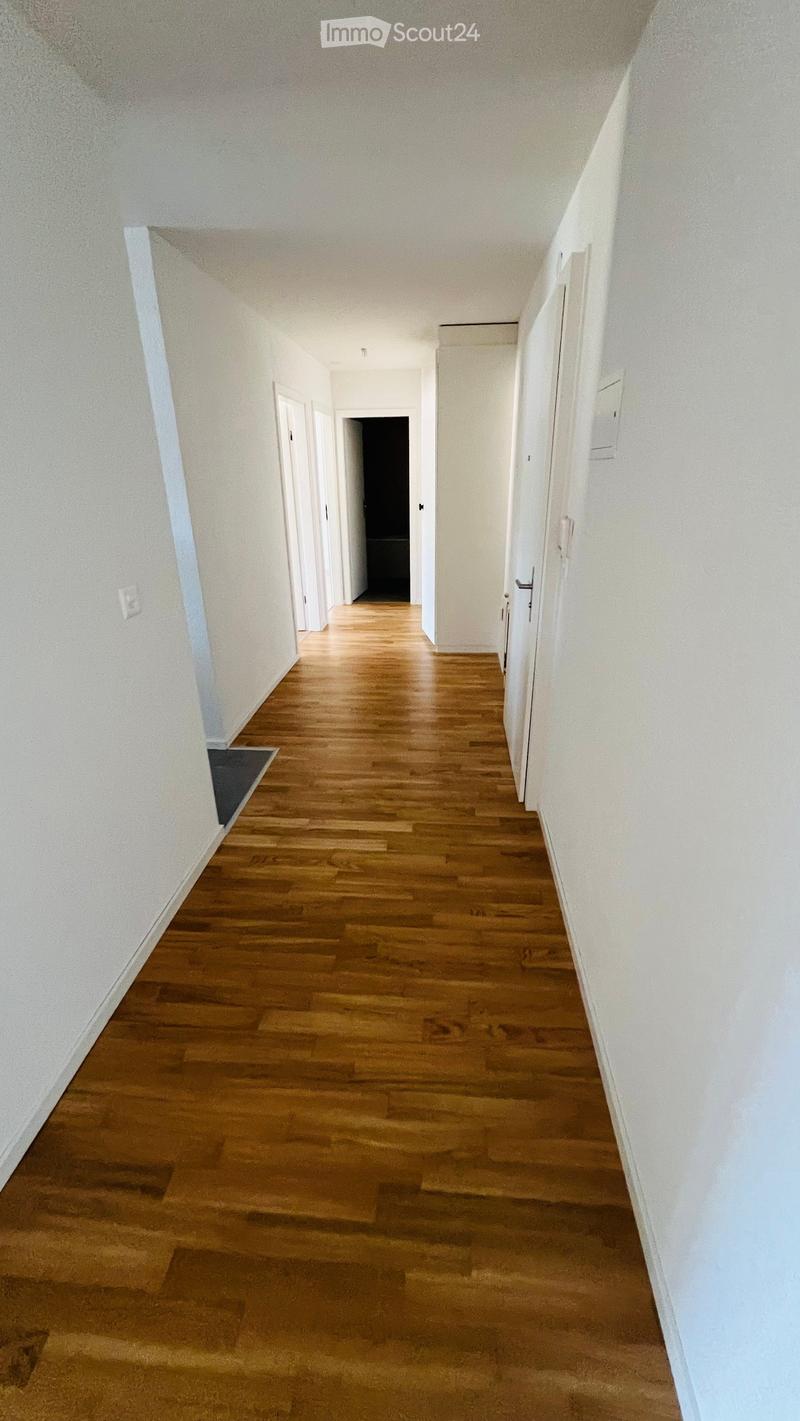 Empty hallway with wooden flooring and white walls, featuring several closed doors on both sides.