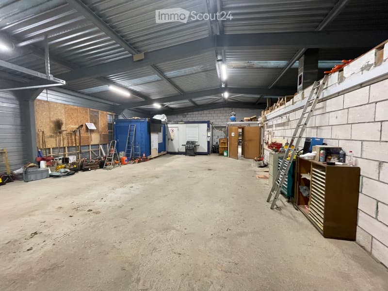 Large, empty workshop or garage space with concrete floor, metal ceiling, and scattered tools and equipment along the walls.