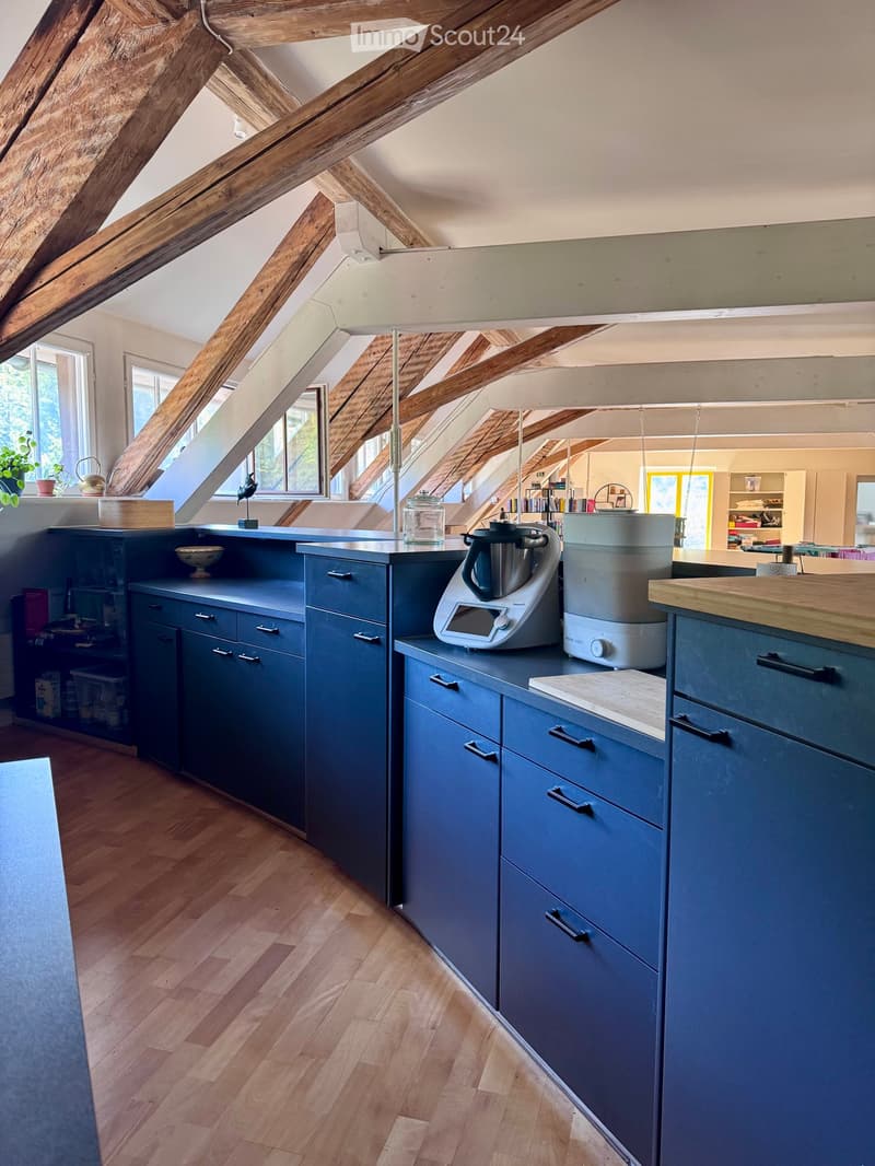 Modern kitchen with dark blue cabinets, wooden countertops, and exposed wooden beams. Features a blender, food processor, cutting board, bowl, teapot, jar, and potted plant on the counter.