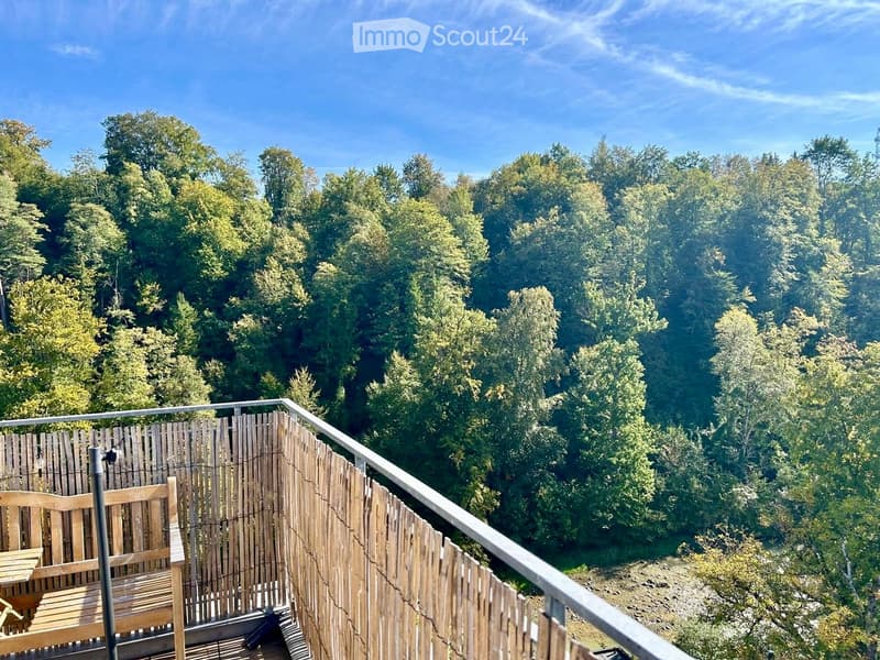 Balcony with wooden railing and a view of a forested area, featuring a wooden bench and table.