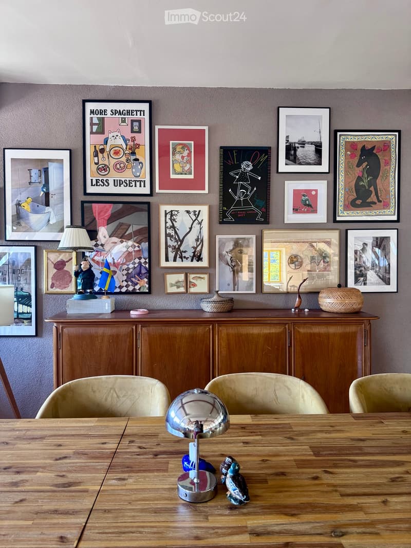 Dining area with wooden table, chairs, cabinet, and various decorative items including framed pictures and a lamp.