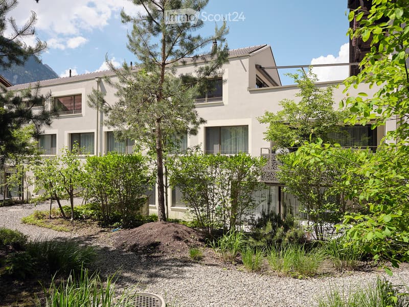 Building. Modern two-story house with white exterior, large windows, and surrounding greenery including trees and shrubs.