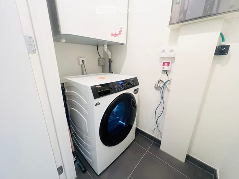 Modern bathroom with a white washing machine, tiled floor, and white walls.