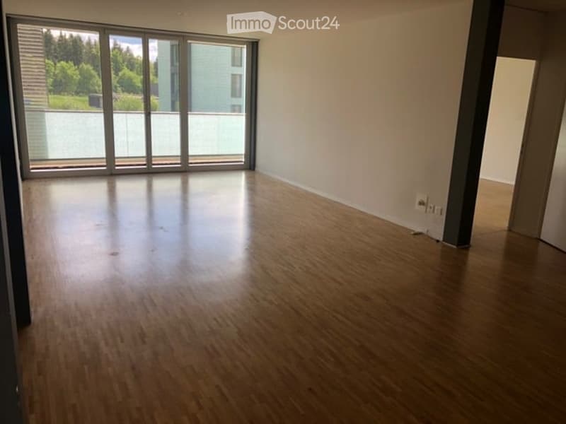 Empty room with wooden flooring and large glass sliding doors leading to a balcony. Bare walls and no furniture.