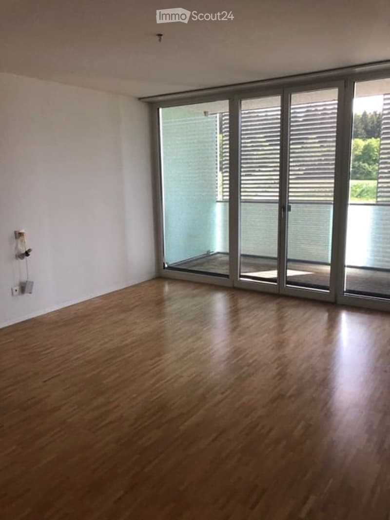 Empty room with wooden flooring and large glass sliding doors leading to a balcony area.