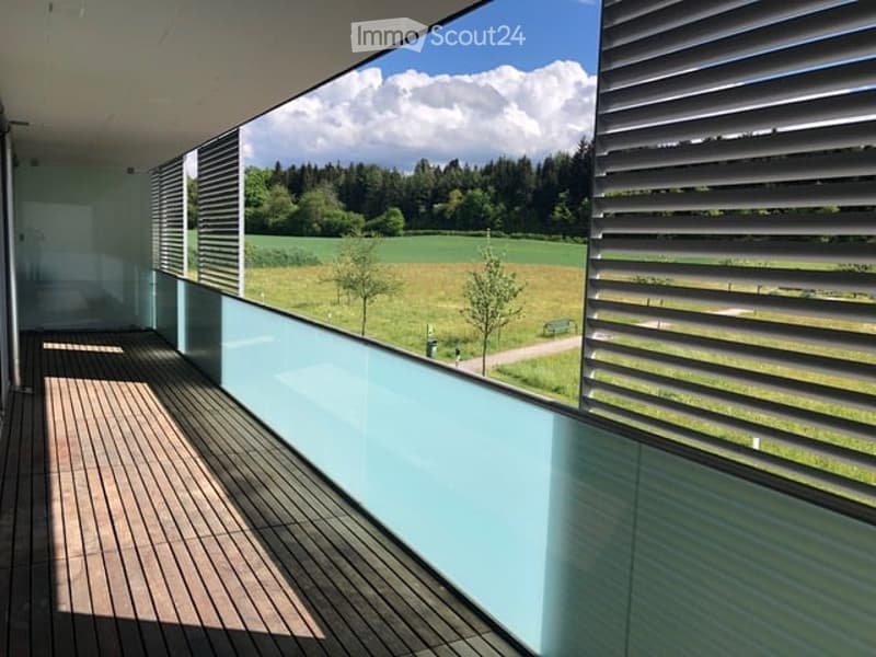 Modern balcony with wooden decking, glass railing, and scenic countryside view.