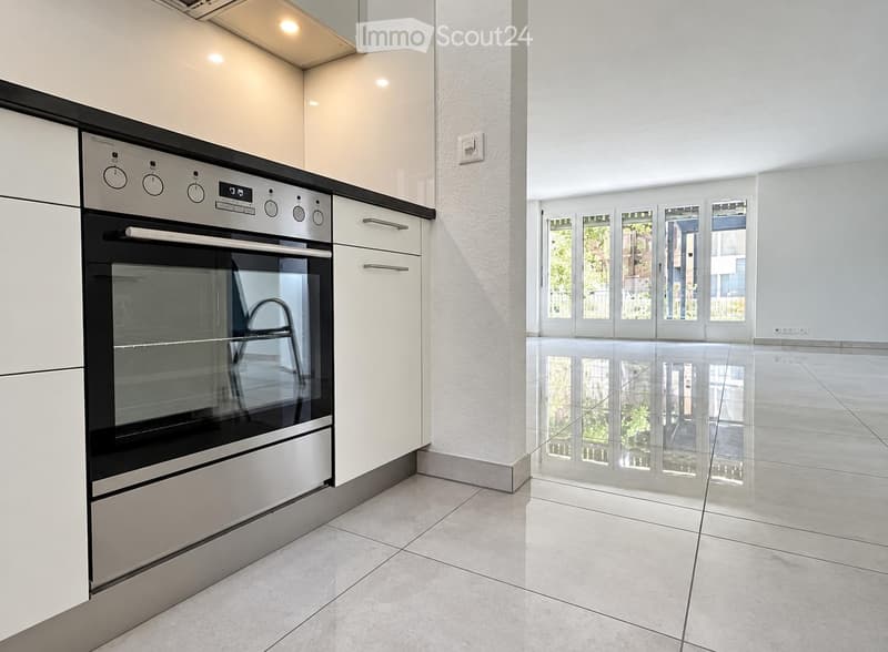 Modern kitchen with white cabinets, stainless steel oven, and large windows leading to a balcony.