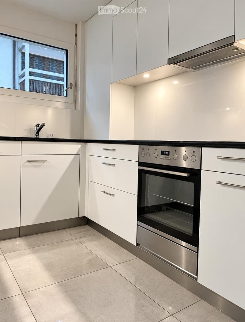 Modern kitchen with white cabinets, stainless steel oven, and tiled floor.