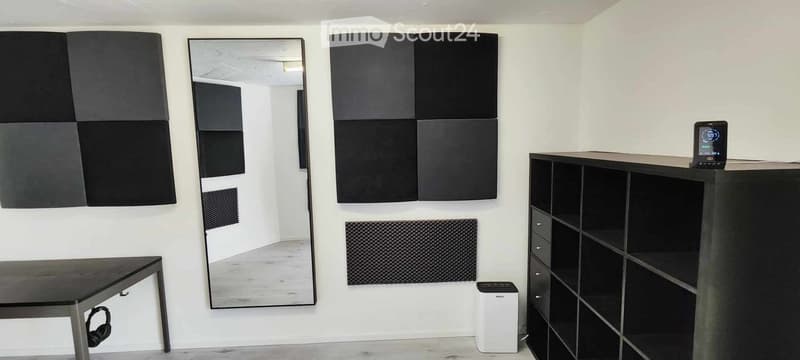 Modern, minimalist room with white walls, a large mirror, acoustic panels, a sleek black table, a shelving unit, and a small white air purifier.