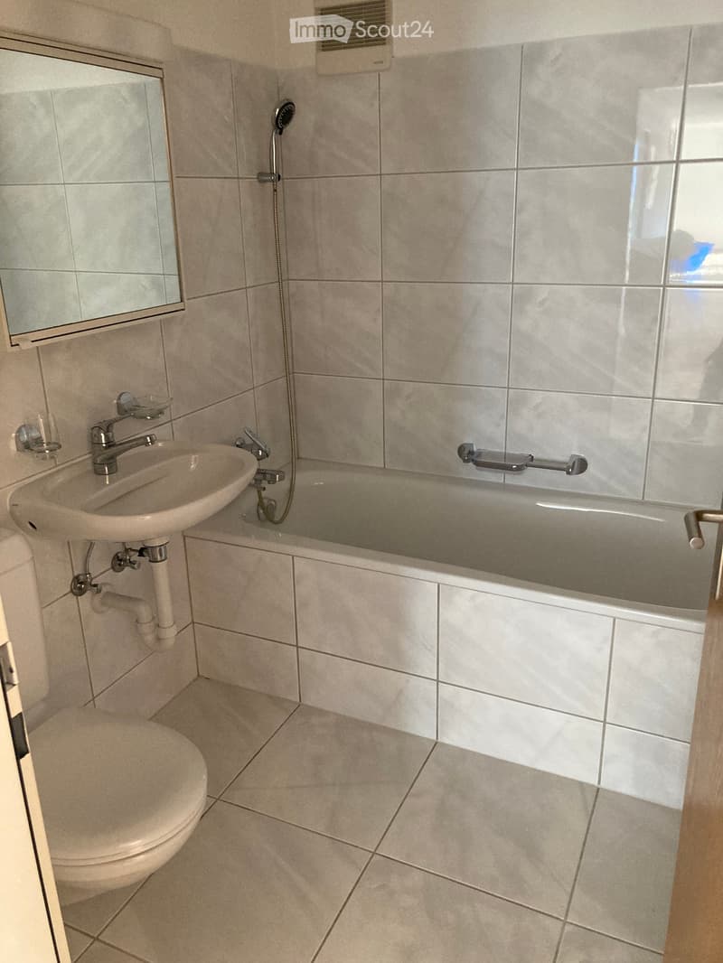 Modern bathroom with beige tiles, a toilet, a sink with a mirror, a bathtub with a showerhead, and a handheld shower attachment.
