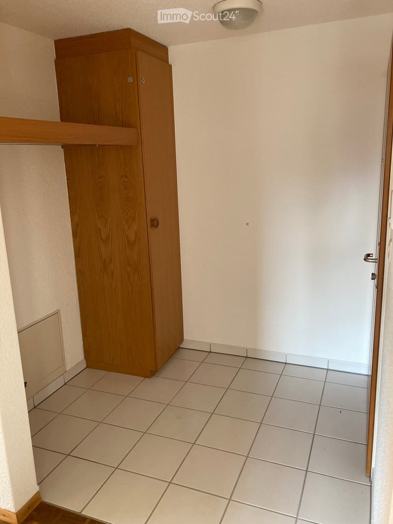 Empty room with tiled floor, wooden cabinet, and white walls.