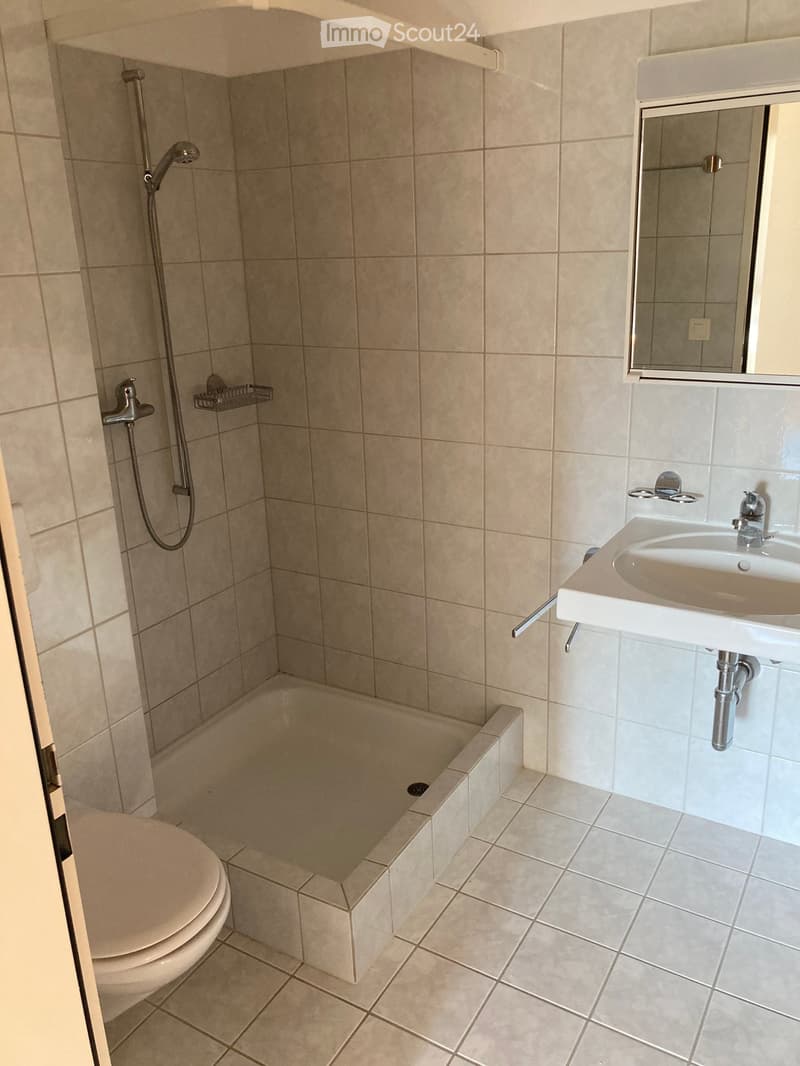 Bathroom with beige tiles, a toilet, a bathtub, a sink with a mirror, and a showerhead.