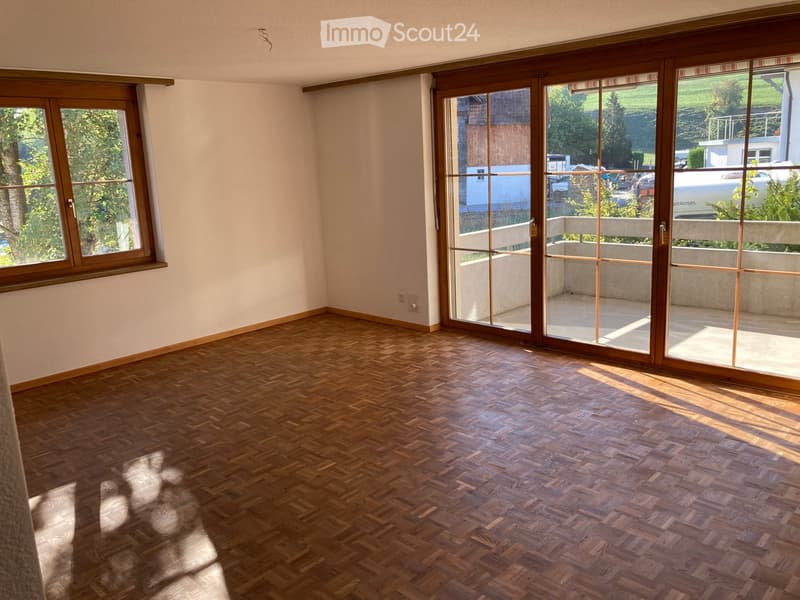 Empty room with wooden parquet flooring, large windows, and sliding glass doors leading to a balcony.