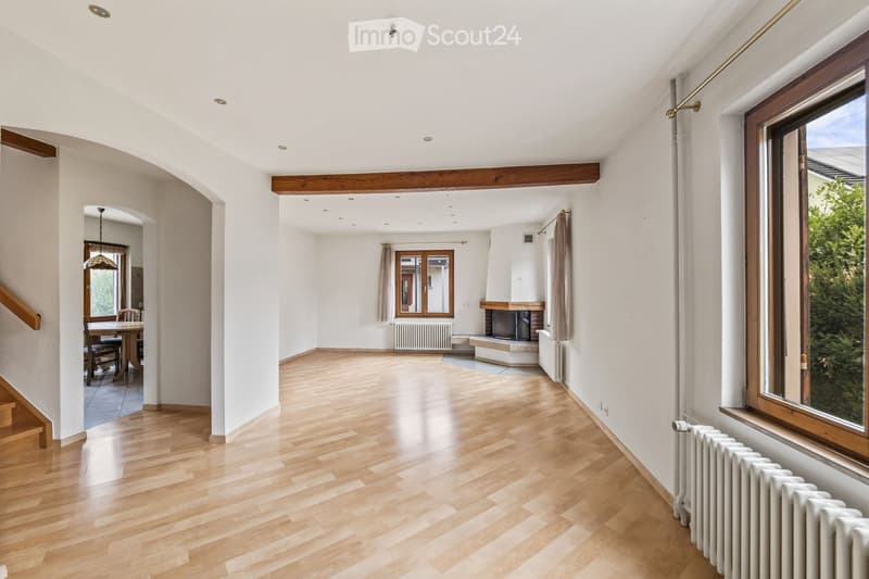 Spacious living room with wooden flooring, fireplace, large windows, dining area with table and chairs, and modern lighting.