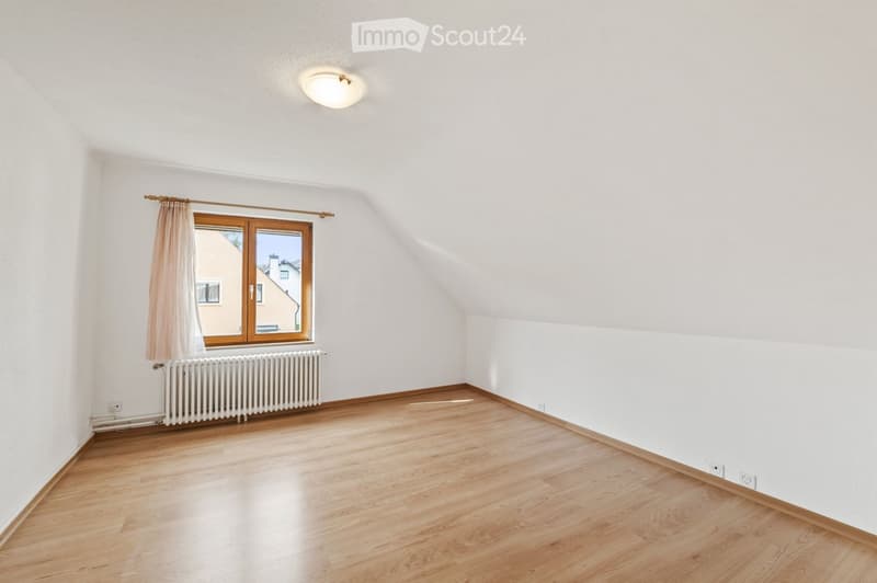 Empty room with wooden flooring, white walls, a window with curtains, a radiator, and a ceiling light fixture.