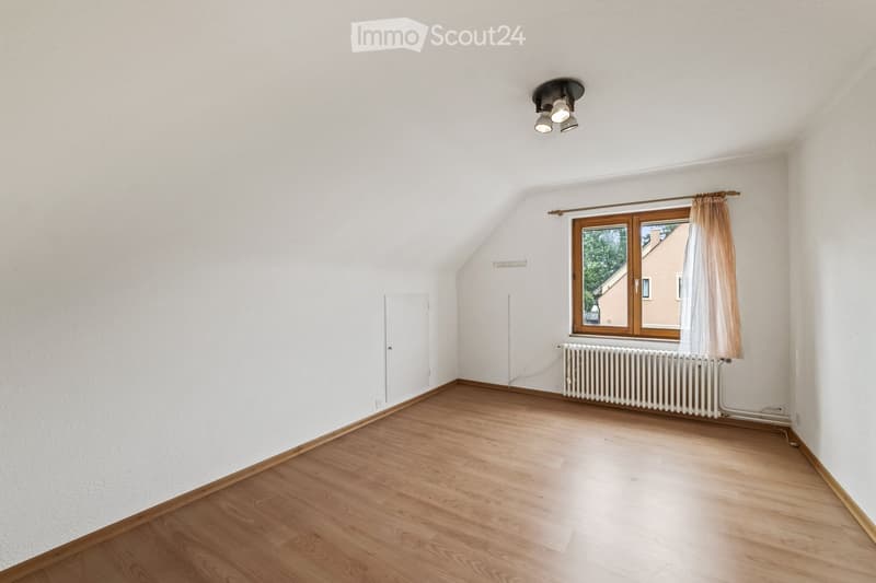 Empty room with wooden flooring, white walls, a window with curtains, a radiator, and a ceiling light fixture.
